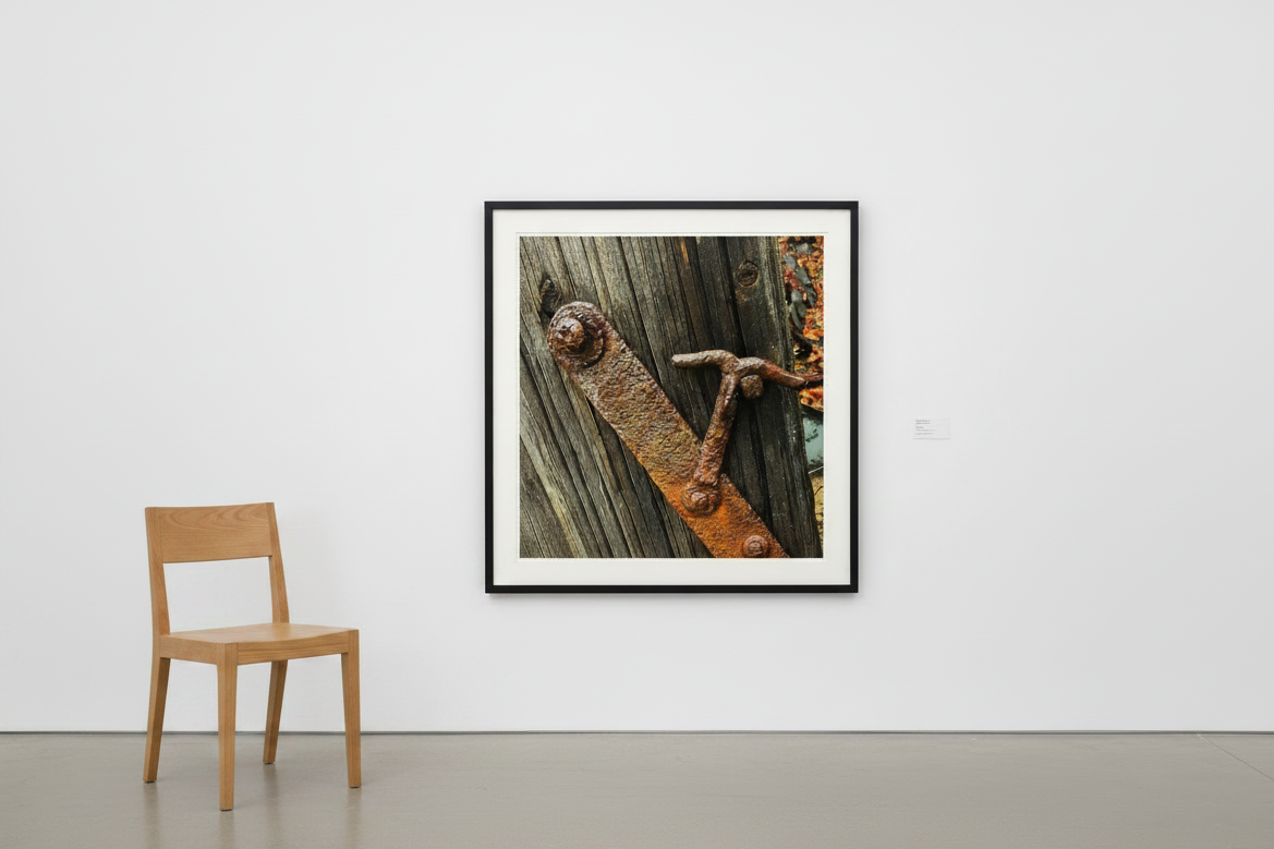 Rusty metal latch on weathered wood, framed wall art print with black frame, displayed beside wooden chair