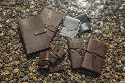 Leather journals and notebooks on pebbled shore with water, rustic handmade style
