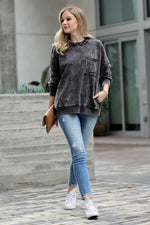 Woman wearing a gray oversized sweater and blue jeans standing on a sidewalk.