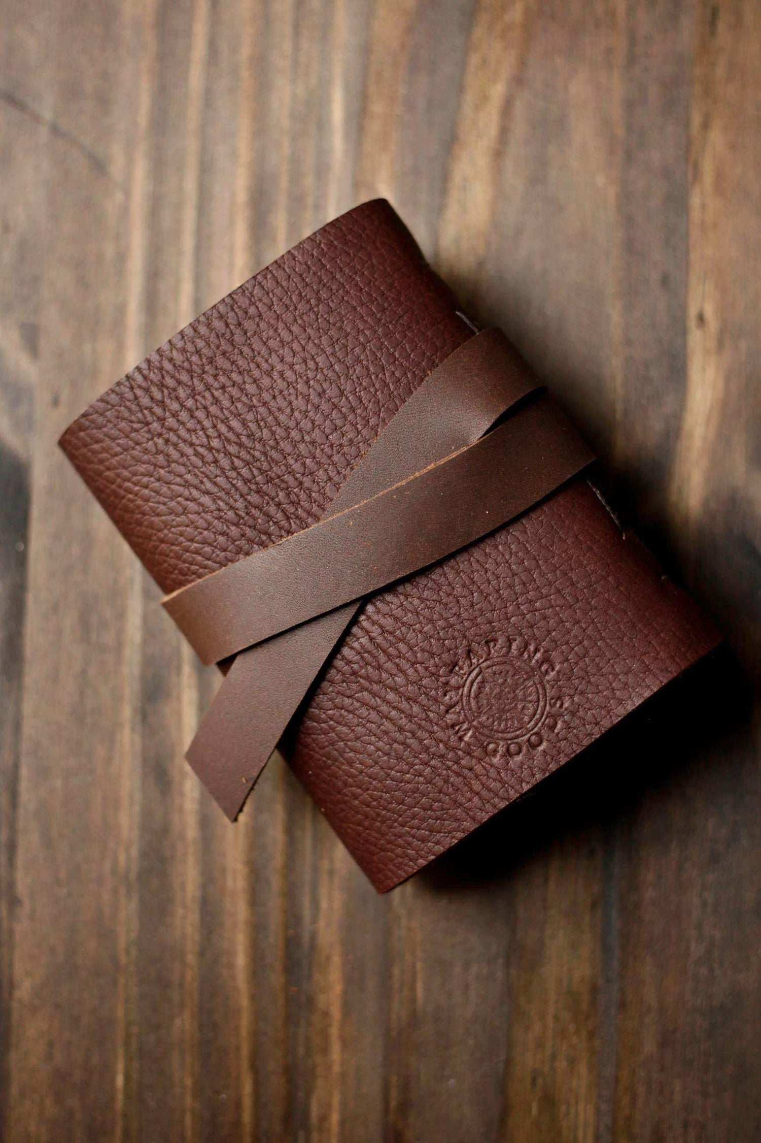 Brown leather wallet with strap closure on wooden surface