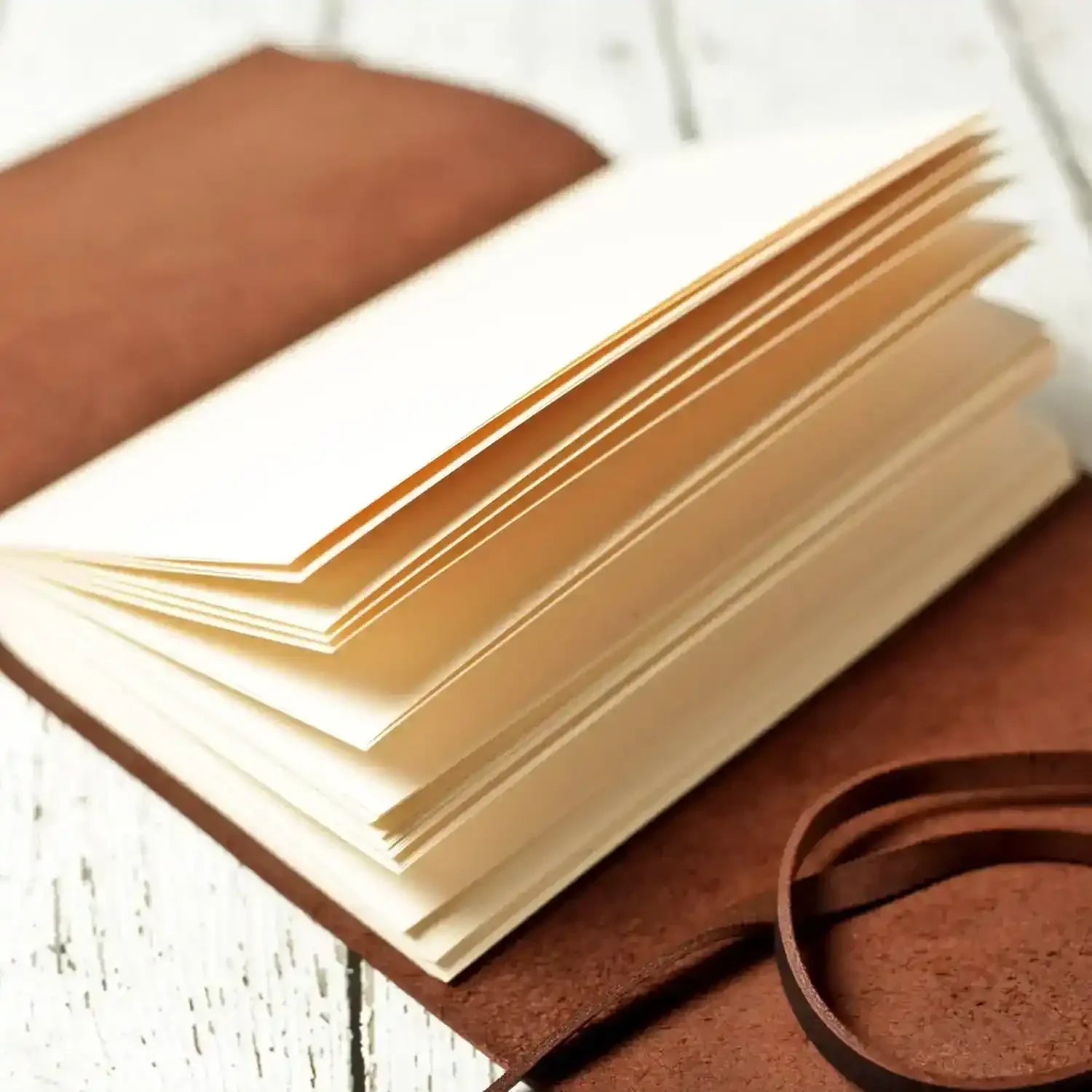 Open leather-bound journal with cream pages on rustic white wood surface