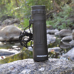Black monocular with 'HUMVEE' branding on a rock by a water body