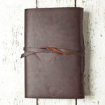 Brown leather journal with strap closure on rustic white wood background