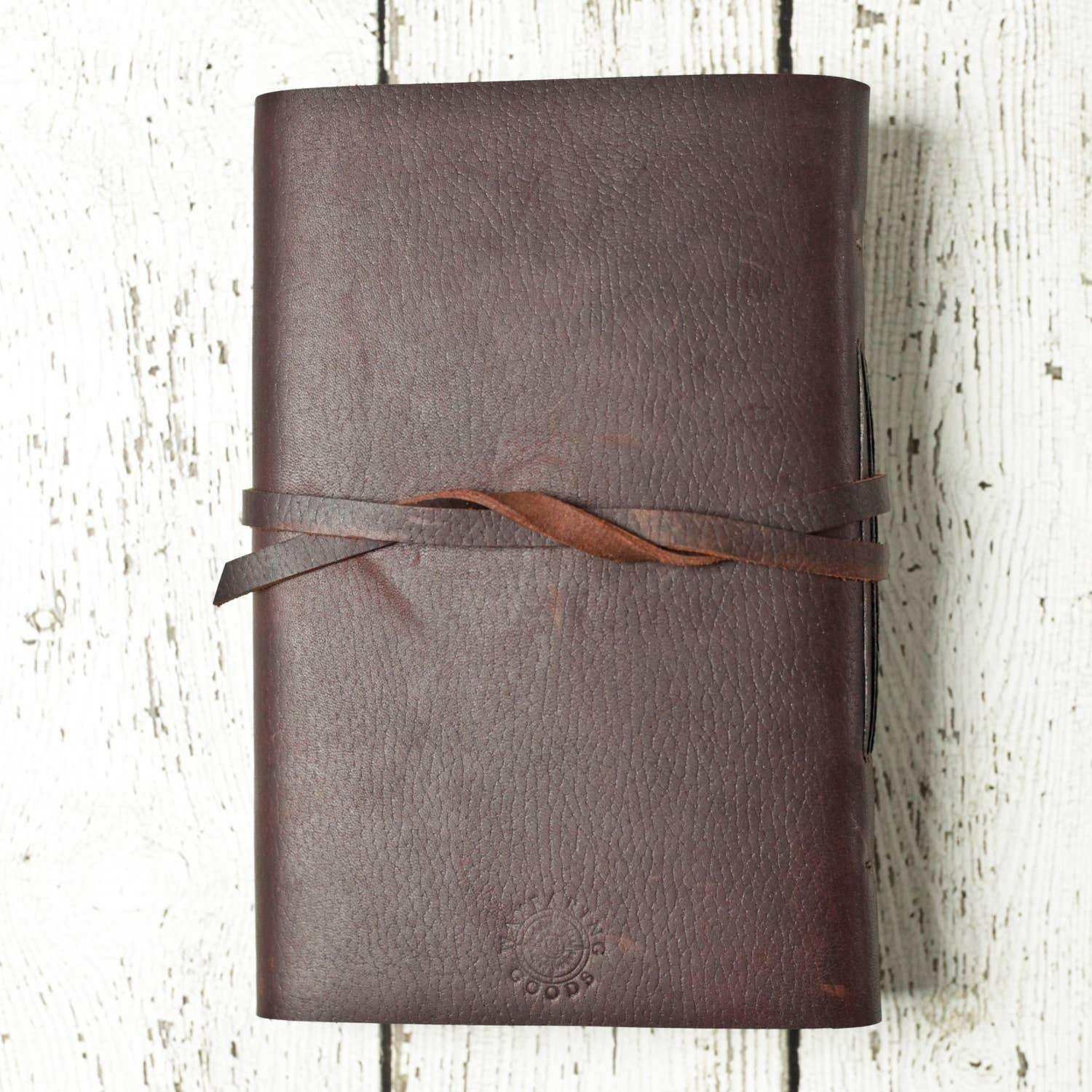Brown leather journal with strap closure on rustic white wood background