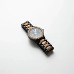 Wooden watch with black and natural wood band, gray dial, and textured bezel on white background
