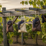 Freshly harvested dark grapes in canvas bags hanging on wooden vineyard trellis at sunset