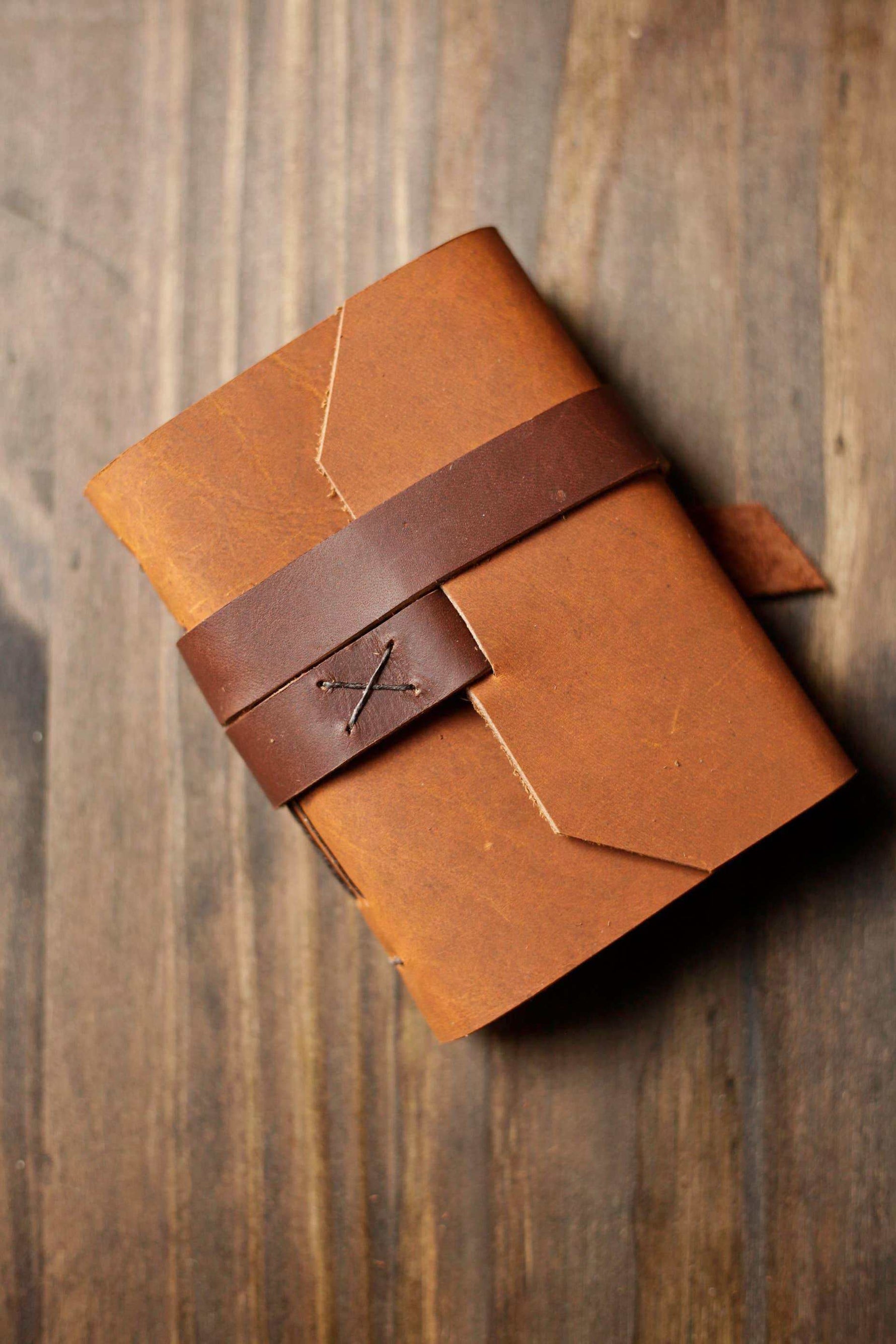 Handmade leather journal with strap closure on rustic wood surface