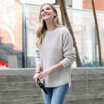 Woman wearing a beige sweater and blue jeans standing outdoors.