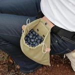 Olive green drawstring pouch filled with fresh blueberries, worn on a person's hip outdoors.
