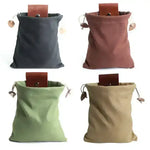 Four canvas drawstring bags in gray, rust, green, and tan with leather accents and wooden toggles