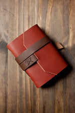 Handcrafted leather wallet with strap closure on rustic wood surface