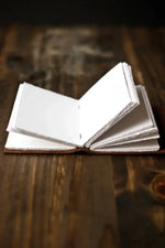 Small open notebook with blank white pages on rustic wooden surface