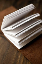 Stack of white art prints with deckled edges on wooden surface, ready for framing