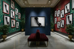 Framed black and white photography art displayed in a gallery with red and green floral walls, marble floor, and velvet bench