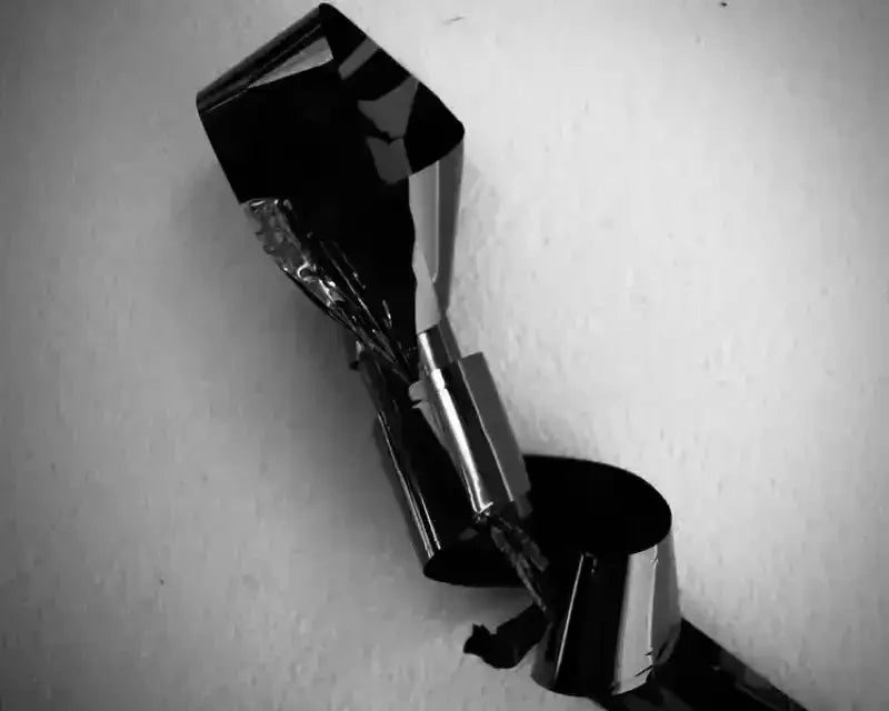 Black and silver metallic ribbon curling against white wall, monochrome abstract photography