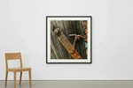 Framed rustic print of weathered wood and rusty metal hardware, displayed on white wall beside wooden chair