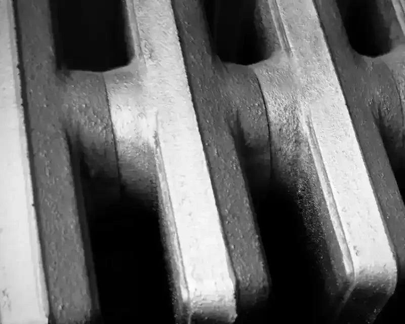Black and white close-up of textured cast iron radiator fins, showcasing industrial detail and shadow contrast.