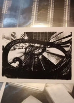 Black and white urban street scene print with ornate metal railing, city buildings, and filmstrip border