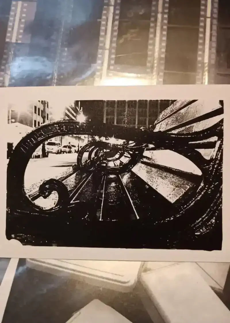Black and white urban street scene print with ornate metal railing, city buildings, and filmstrip border