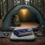 Camping scene with a tent, sleeping pad, and folded blanket in a forest setting.
