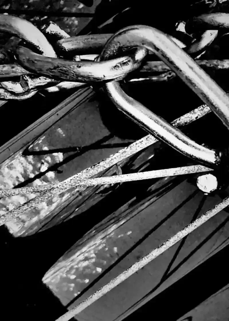 Black and white close-up of rustic metal chain links and weathered wood, textured industrial photography