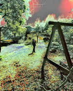 Infrared landscape photo with vibrant green grass, red sky, and wooden swing set in a backyard