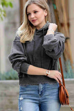 Woman wearing a gray sweater and blue jeans with a brown leather bag outdoors.