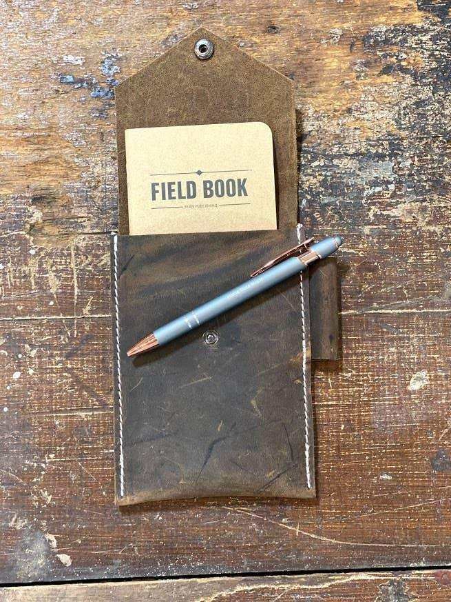Leather field notebook holder with pen, rustic wood background