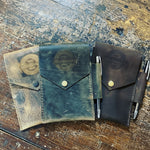 Handcrafted leather pen cases with snap closures, displayed on rustic wood surface