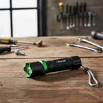 Black and green flashlight on a wooden workbench with tools in the background