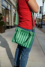 Green striped crossbody bag with adjustable strap worn on city sidewalk