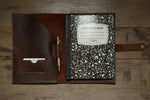 Leather notebook cover with pen holder and composition book on rustic wood