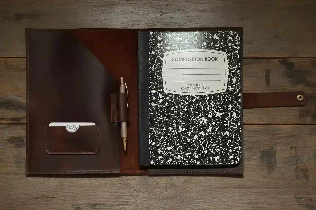 Leather notebook cover with pen holder and composition book on rustic wood