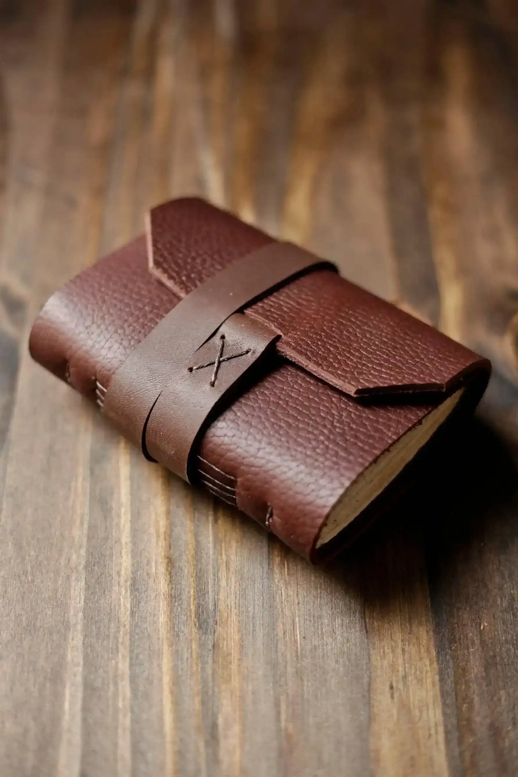 Handmade leather journal with strap closure on rustic wood surface