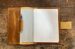 Open leather journal with lined pages and pen, resting on rustic wooden surface