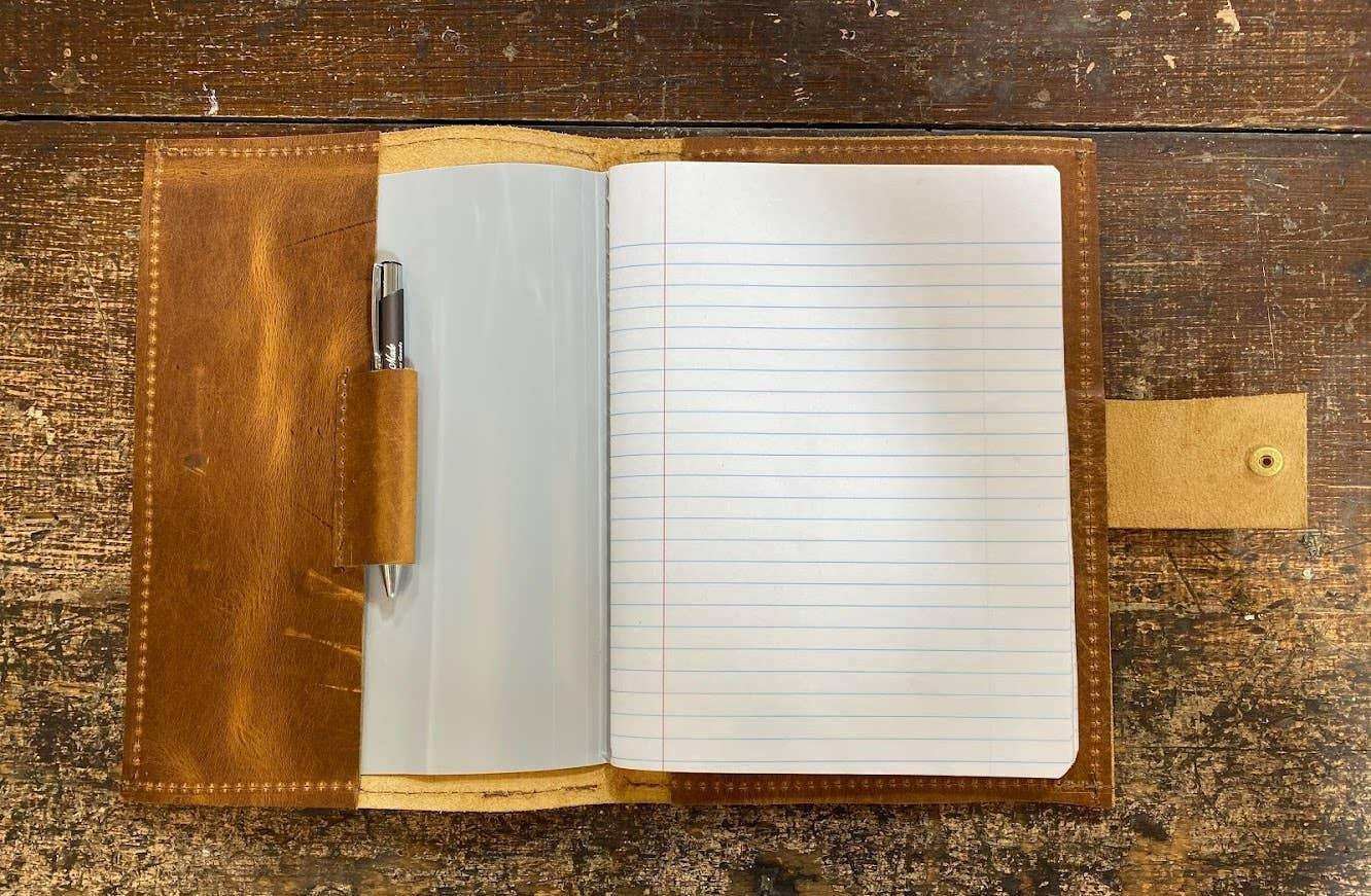 Open leather journal with lined pages and pen, resting on rustic wooden surface