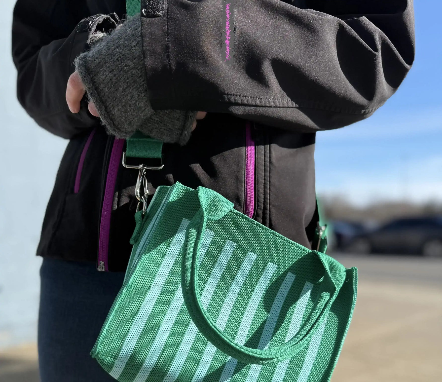 Person holding green striped tote bag with black jacket and gloves outdoors