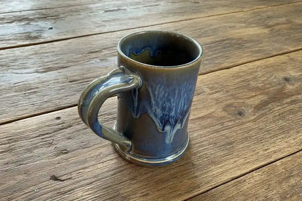 Handmade ceramic mug with blue and gray drip glaze on rustic wood table
