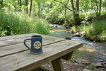 mugs left handed on a picnic table near a stream Mugs
