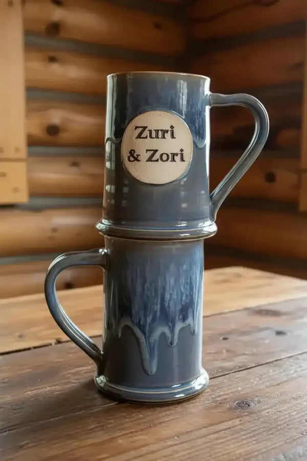 Zuri & Zori ceramic mugs stacked on wooden table, rustic log cabin background