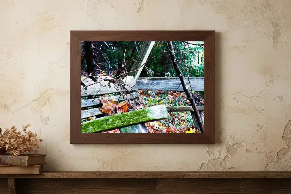 Framed nature print of rustic wooden bridge with autumn leaves, displayed on textured wall beside vintage books