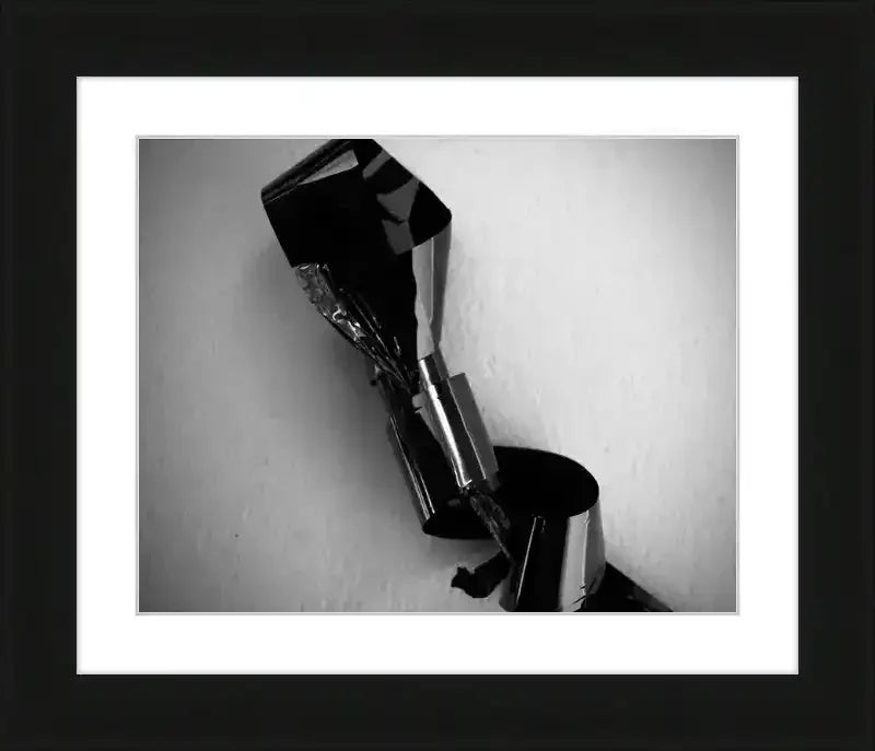 Black and white framed print of abstract metallic sculpture with reflective surfaces and textured wall background