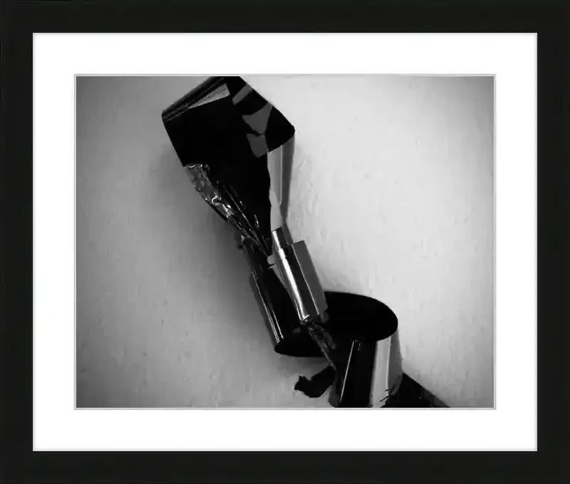 Black and white abstract photography print in black frame, featuring metallic sculpture against textured wall