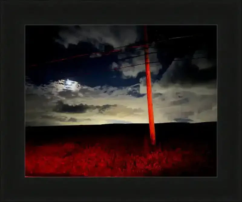 Dramatic night sky with glowing moon, dark clouds, and red-lit utility pole over shadowed field, framed print