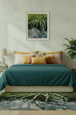 Framed nature print of green foliage above bed, matching rug, cozy bedroom decor with teal bedding and plants