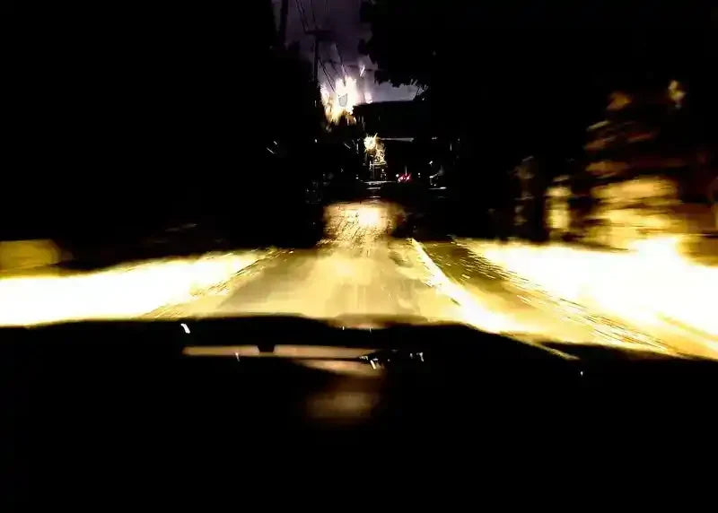 Nighttime road view from car headlights, wet pavement reflecting light, blurred motion