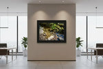 Framed nature print of mossy stream with rocks, displayed in modern office with city view windows