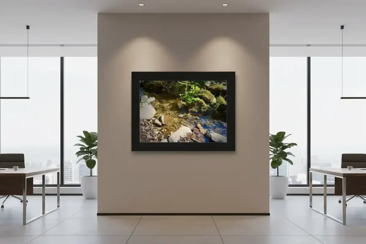 Framed nature print of mossy stream with rocks, displayed in modern office with city view windows