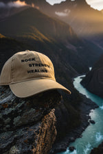 Beige cap with 'Rock Strength Healing' text Mountain background