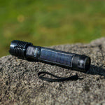 Black flashlight with solar panel on a rock with green grass in the background